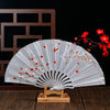 Elegant white folding fan with red plum blossoms displayed on a wooden stand.