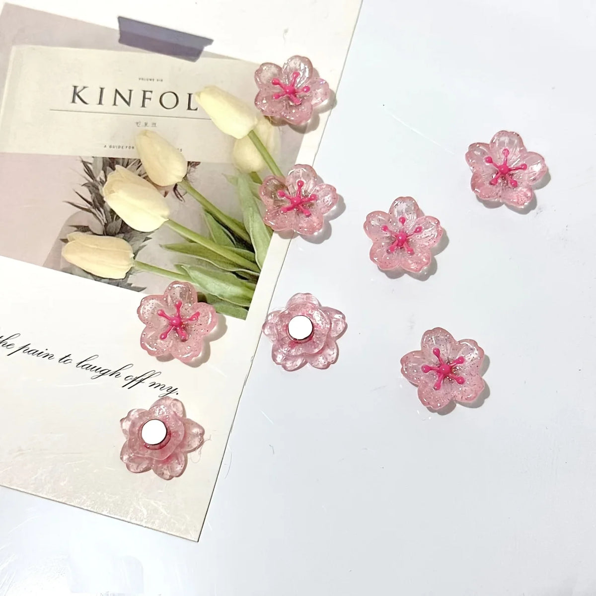 A collection of pink and white decorative cherry blossom fridge magnets displayed on a light background.