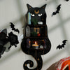 A black cat silhouette decoratively mounted on a floating shelf displaying crystals, moss, and candles.