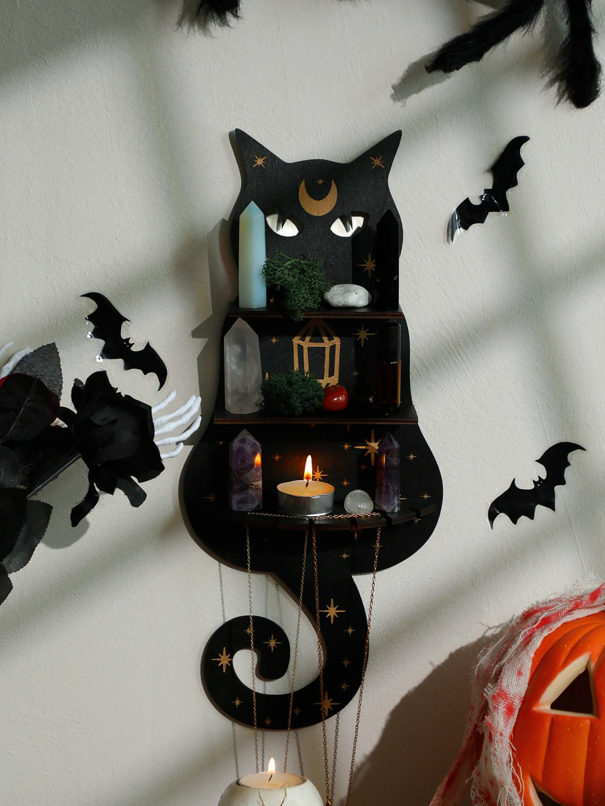 A black cat silhouette decoratively mounted on a floating shelf displaying crystals, moss, and candles.