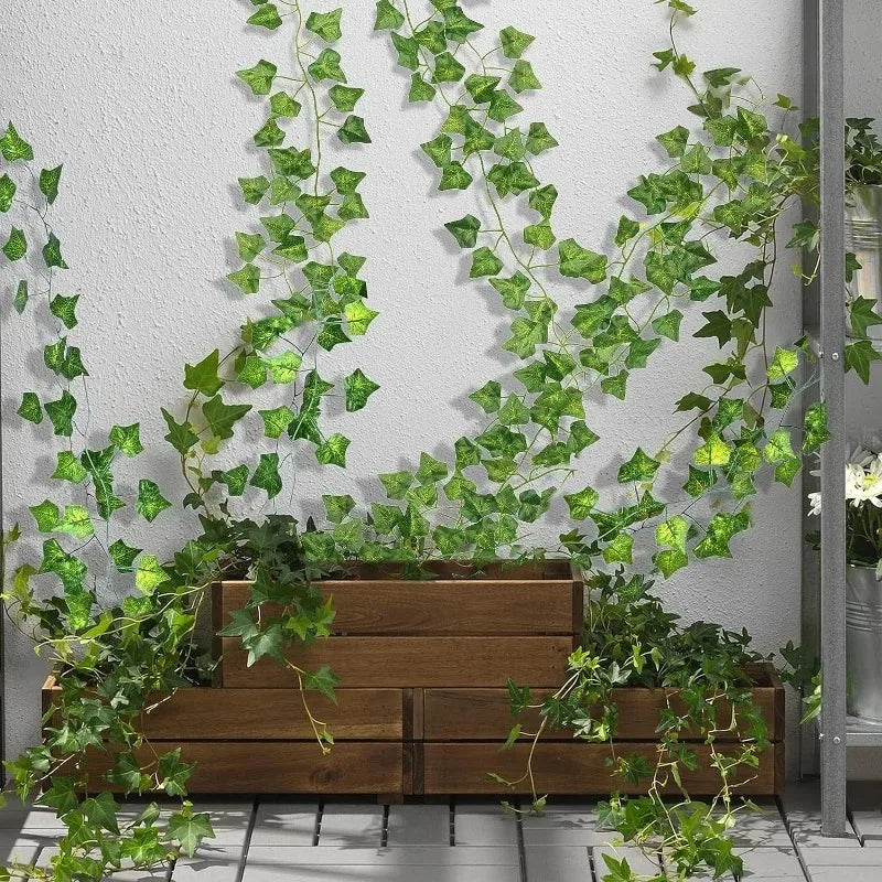 Artificial ivy vine garland cascading over a wooden planter against a gray wall.