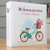 A white photo album titled Mi Álbum de Fotos Creando historias featuring a teal bicycle with pink flowers.