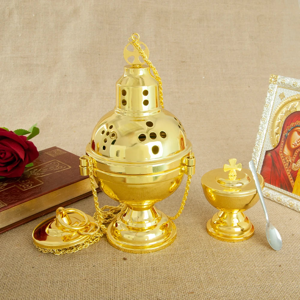 A gold-plated Orthodox censer with bells resting on a beige cloth next to a small spoon.