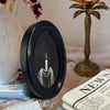 A black oval candle holder with a white candle and a depiction of hands in a dark background.