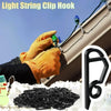 A hand wearing an orange glove is clipping a light string hook onto a building exterior, with a pile of black clips nearby.