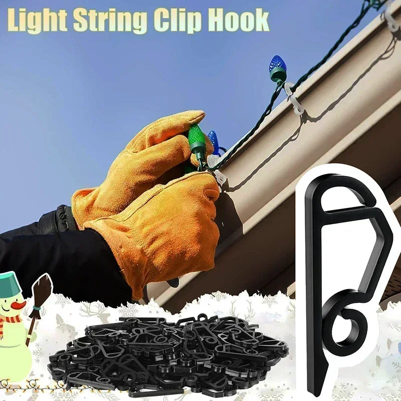 A hand wearing an orange glove is clipping a light string hook onto a building exterior, with a pile of black clips nearby.