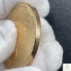A gold souvenir coin is held in a white glove against a dark background.