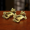 Antique brass sleeping frog figurine in a relaxed pose resting on a wooden surface.