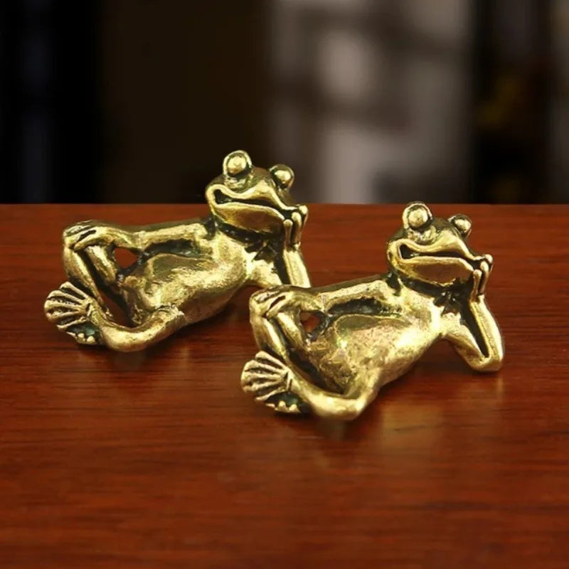 Antique brass sleeping frog figurine in a relaxed pose resting on a wooden surface.