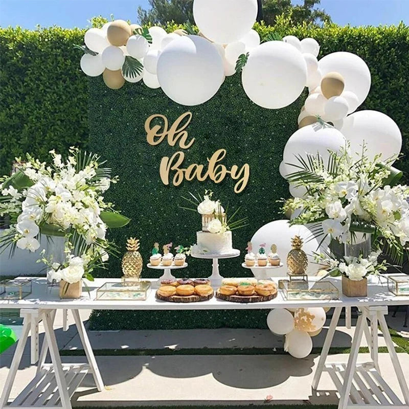 A wooden sign spelling out Oh Baby decorated with white balloons and floral arrangements for a baby shower.