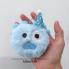 A light blue fluffy plush doll with a conical blue hat and a white pompom, held in a hand.
