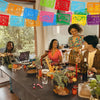 A group of people celebrating with a colorful papel picado bunting banner strung across the background.