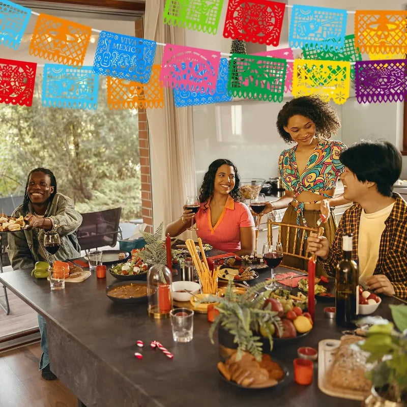 A group of people celebrating with a colorful papel picado bunting banner strung across the background.