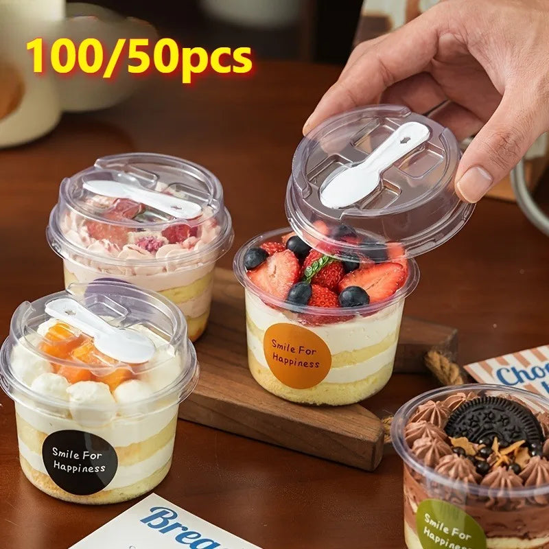 A hand holds a clear reusable pudding cup filled with layered dessert, next to other cups and a wooden board.
