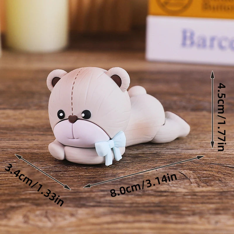 A light pink baby block cake topper shaped like a cute bear with a blue bow.