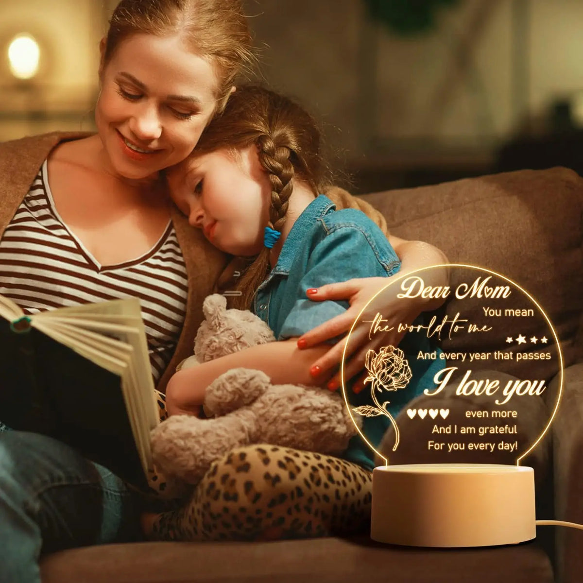 A young woman is reading a book while a little girl rests her head on her shoulder, illuminated by a warm glow night light.