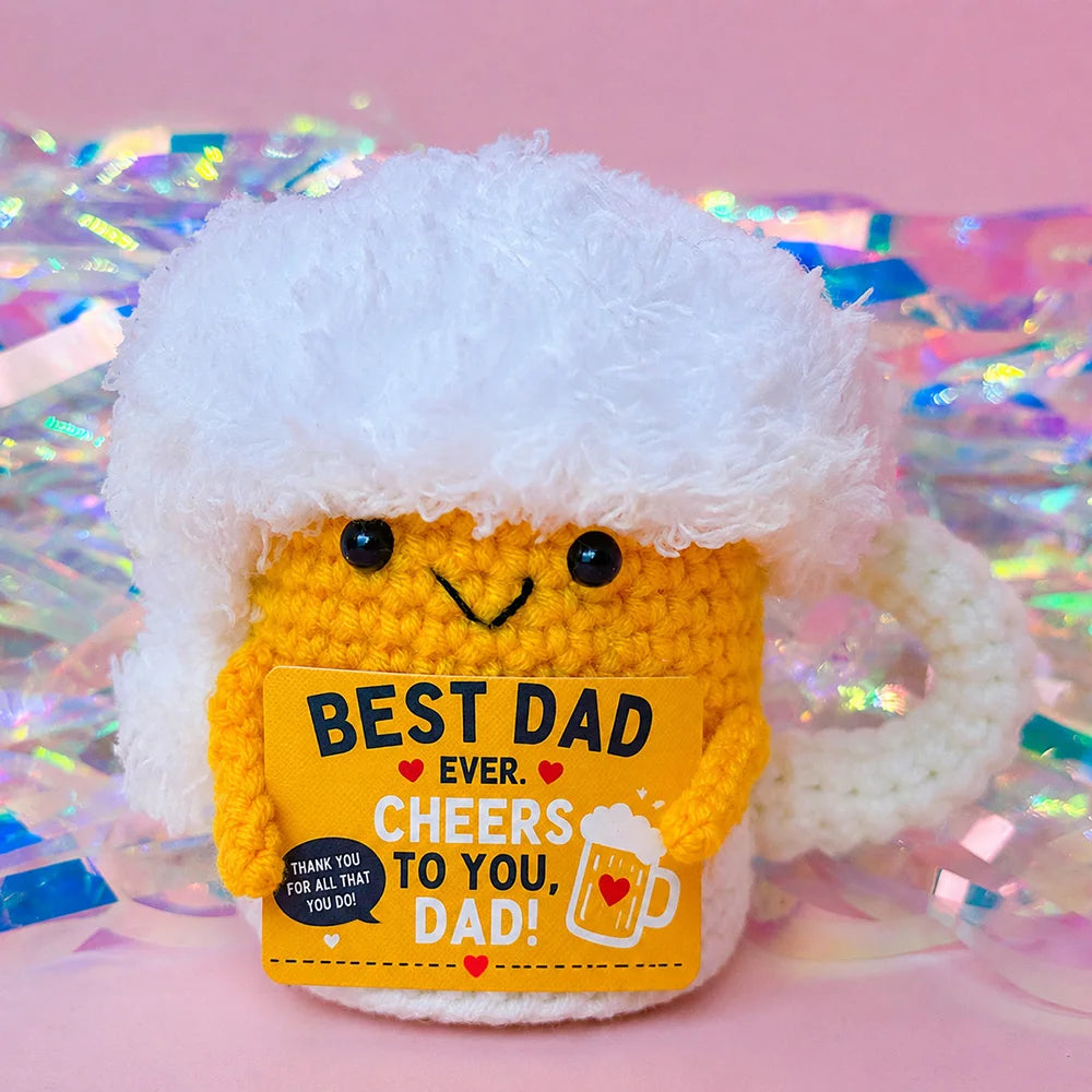 A handcrafted yellow crochet dog doll wearing a white fluffy hat, presented against a sparkly background.
