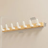 A walnut wood coat rack with eight white hooks and a storage shelf mounted on a light wall.