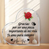 A heart-shaped glass frame with a floral design and Spanish text inside, displayed on a wooden surface.