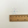 Silver frosted snowflake confetti measured against a wooden ruler.