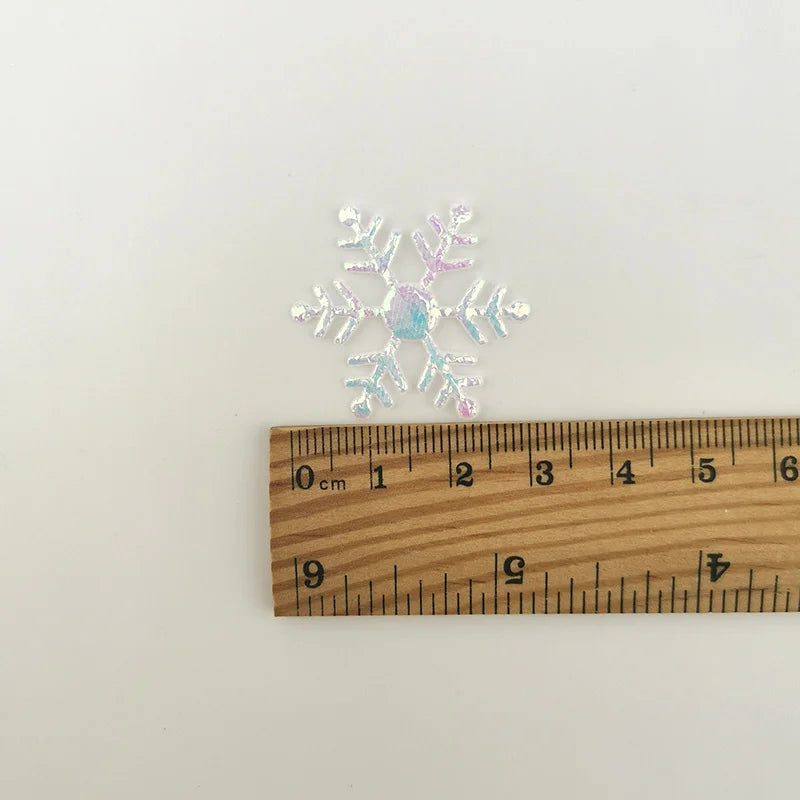 Silver frosted snowflake confetti measured against a wooden ruler.