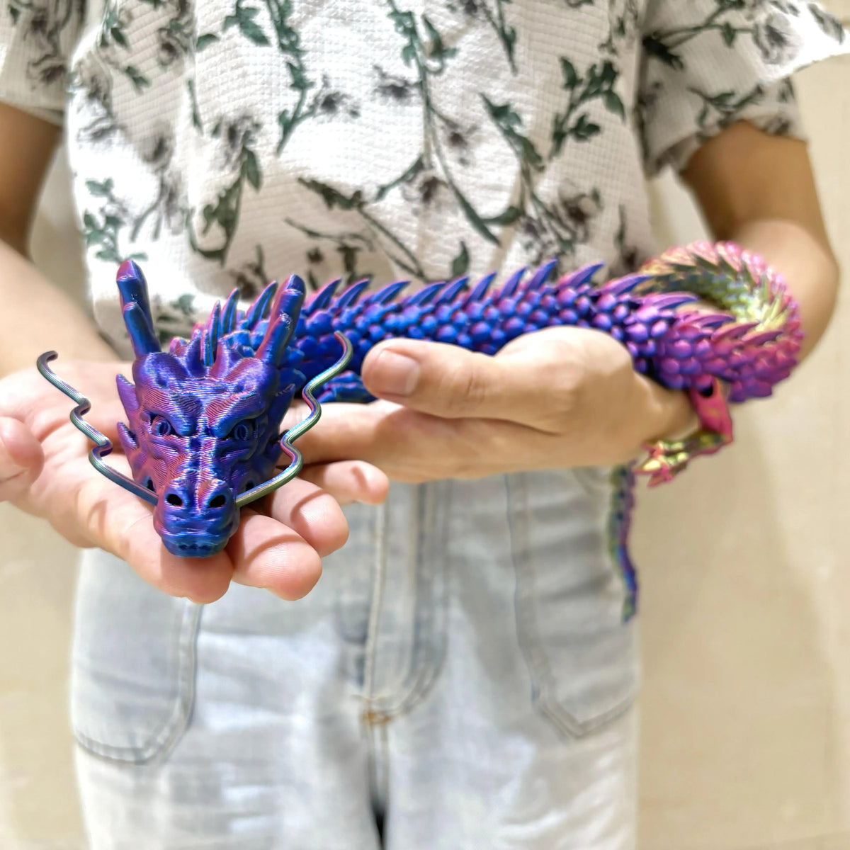 A hand holds a purple and green articulated 3D printed dragon figurine.