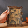 A hand holds a vintage resin photo frame decor with an aged, sepia-toned background featuring dark bamboo silhouettes.