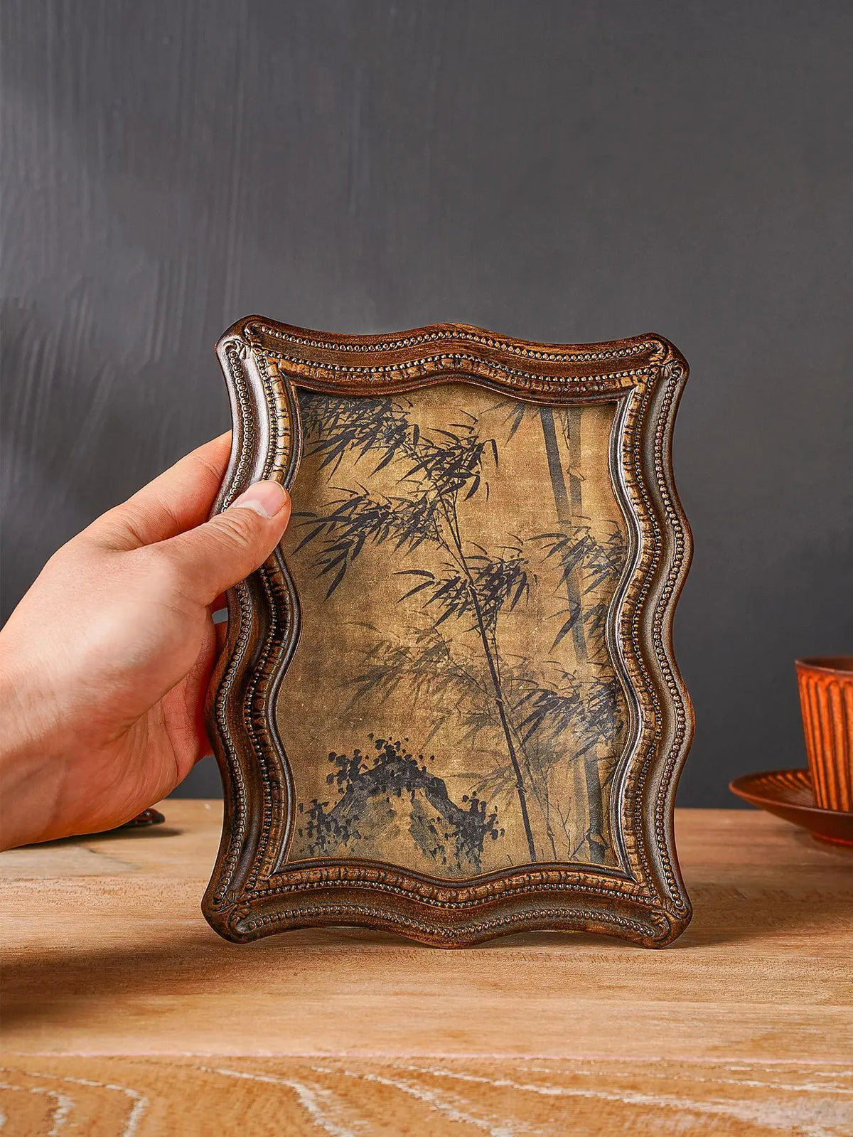 A hand holds a vintage resin photo frame decor with an aged, sepia-toned background featuring dark bamboo silhouettes.