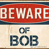 Vintage retro Metall-Dosenwandschild mit einem roten Oval-Warnschild, auf dem steht: 'BEWARE OF BOB'