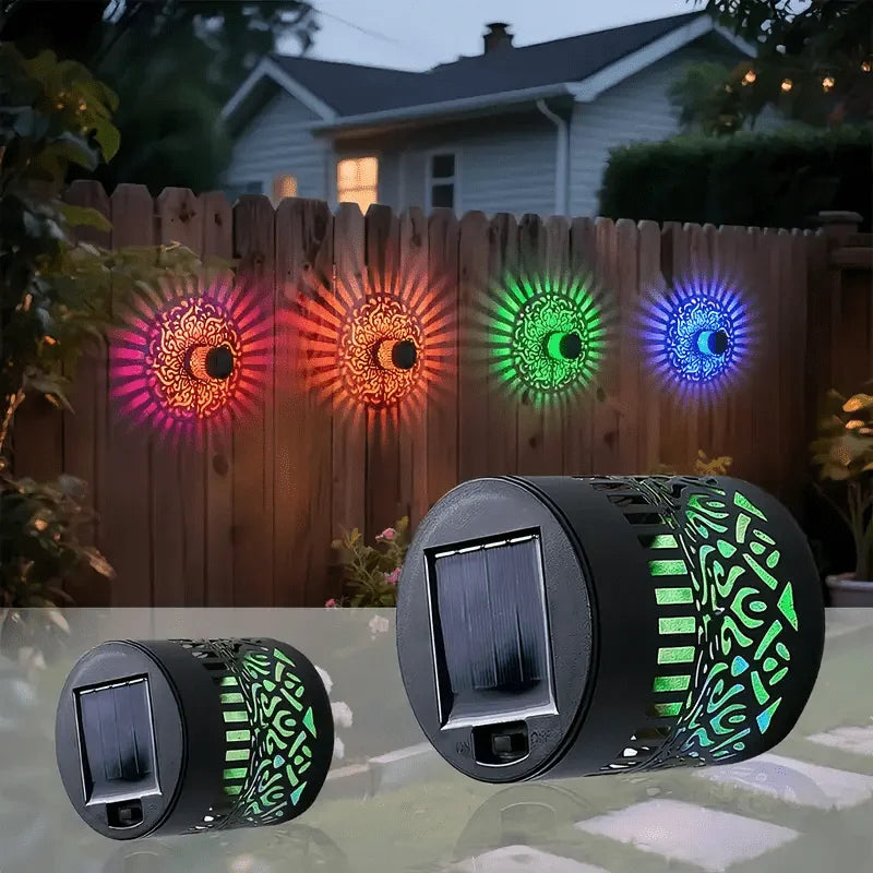 A solar-powered mandala wall lantern displays colorful light patterns on a wooden fence.