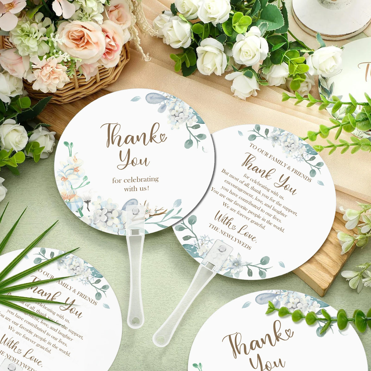 A set of floral message wedding thank you fans with delicate greenery and white roses on a light background.