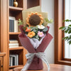 A handmade sunflower daisy crochet bouquet wrapped in a mauve paper and tied with a white ribbon.