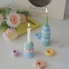A tall white candle in a light blue ceramic holder surrounded by various pastel-colored wax candles and decorative elements.