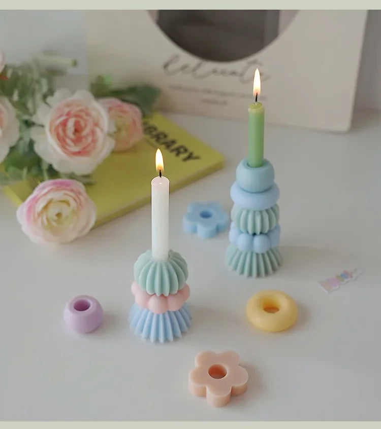 A tall white candle in a light blue ceramic holder surrounded by various pastel-colored wax candles and decorative elements.