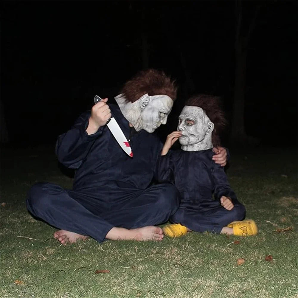 Two individuals dressed as zombies with pale makeup and bloody knife props lying on grass at night