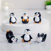 A collection of cute cartoon penguin resin figurines in black and white with orange accents displayed on a white surface.
