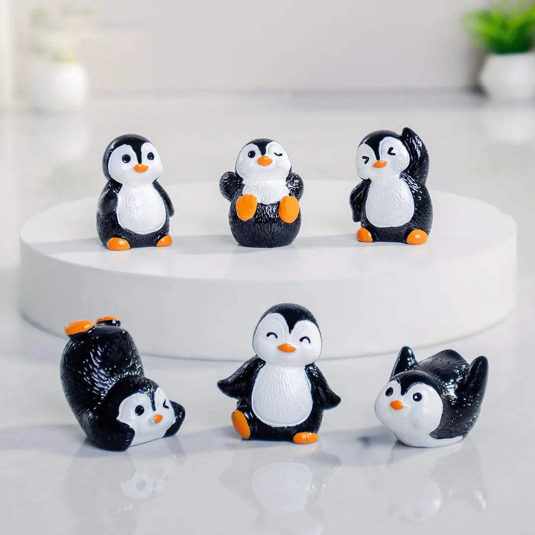 A collection of cute cartoon penguin resin figurines in black and white with orange accents displayed on a white surface.