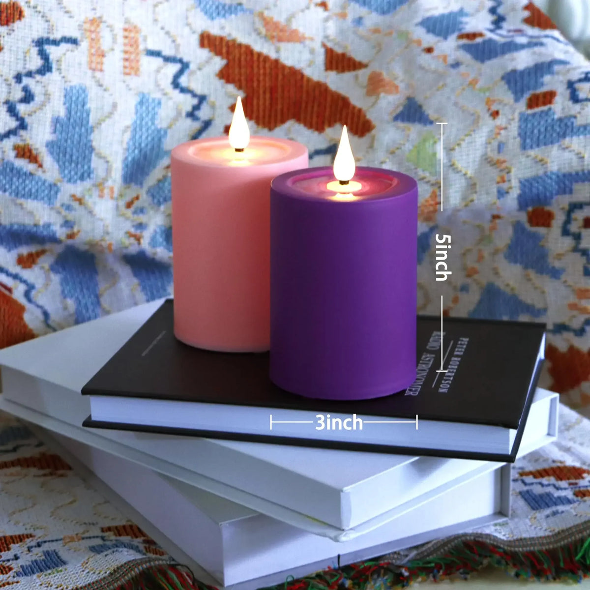A purple flameless LED candle in a holder sits on a stack of white books with a pink candle nearby.