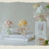 A white candle in a glass jar with a pink ribbon and a white tulip flower is displayed on a stack of books.