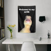 A black flag hangs on a wall with white text that reads Welcome to my crib and features a yellow animal face.