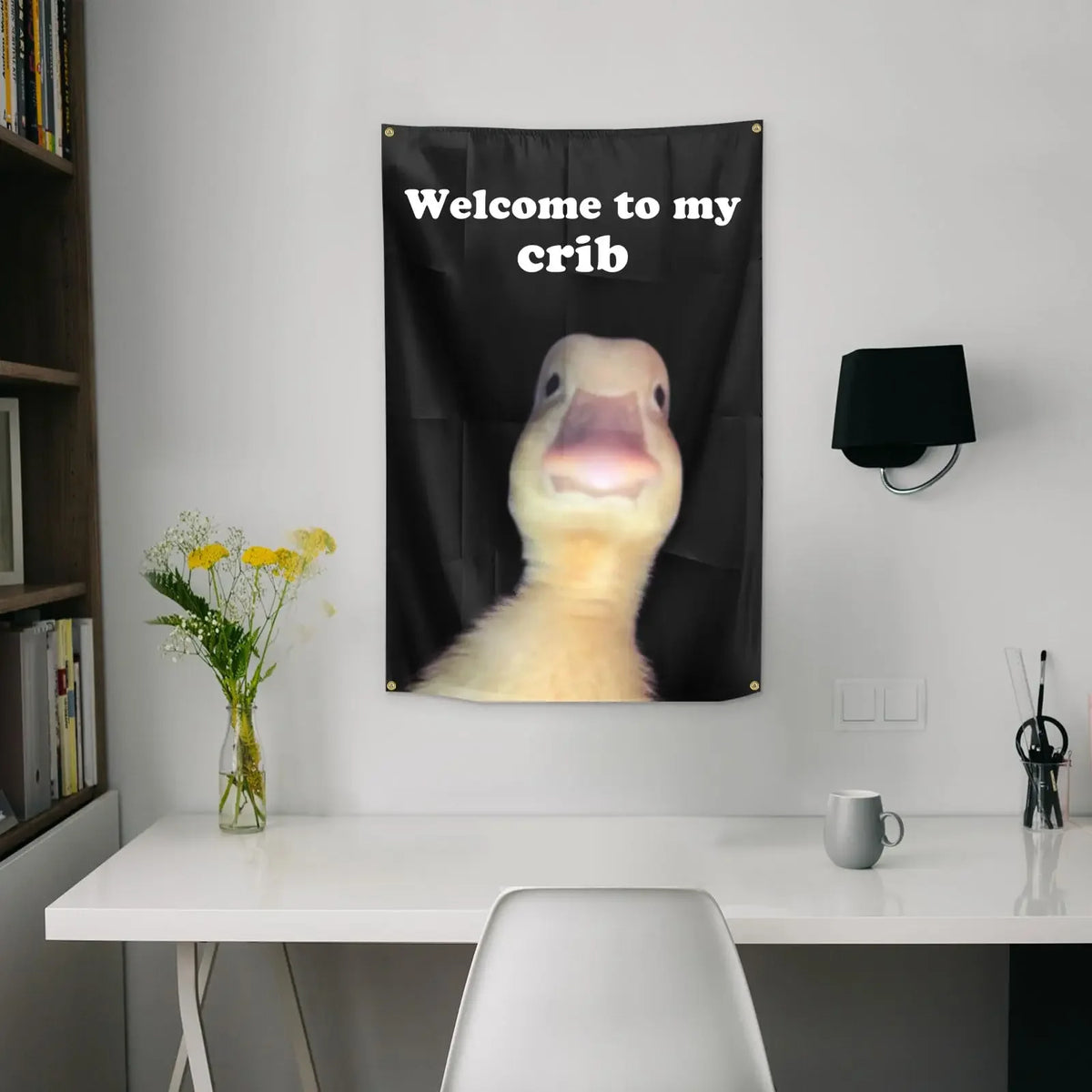 A black flag hangs on a wall with white text that reads Welcome to my crib and features a yellow animal face.