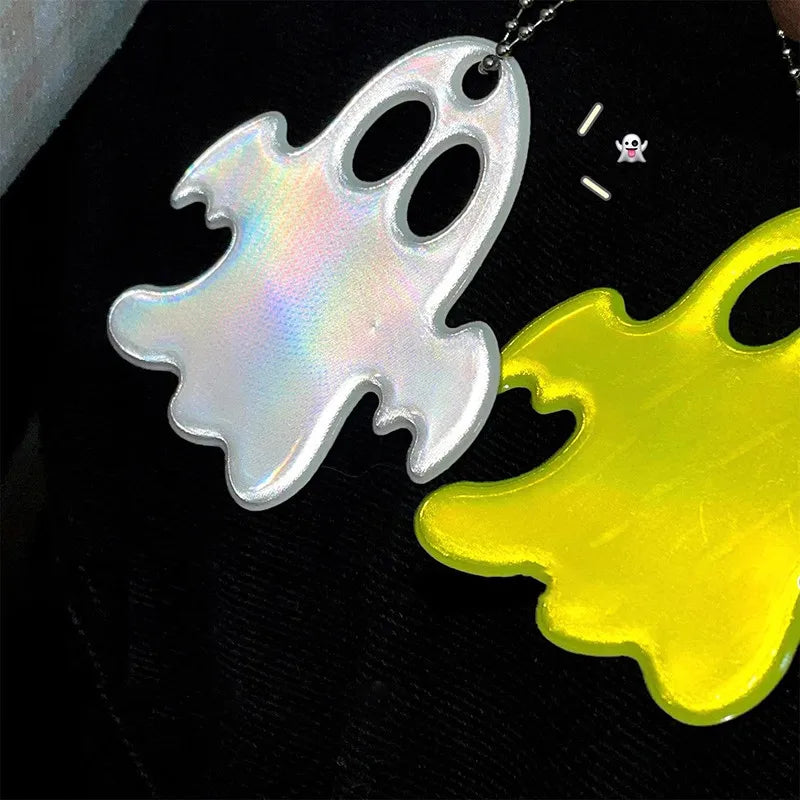 A set of two ghost-shaped reflective keychains, one white and one yellow, displayed against a black background.
