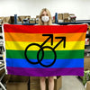 A person holds a horizontal Pride flag displaying the rainbow colors and a black gender symbol.