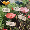 A collection of pink, yellow, and red flowers on wooden sticks used as decorative bee and butterfly watering stations in a ga