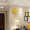 A modern circular gold wall clock with Arabic numerals mounted on a beige wall.