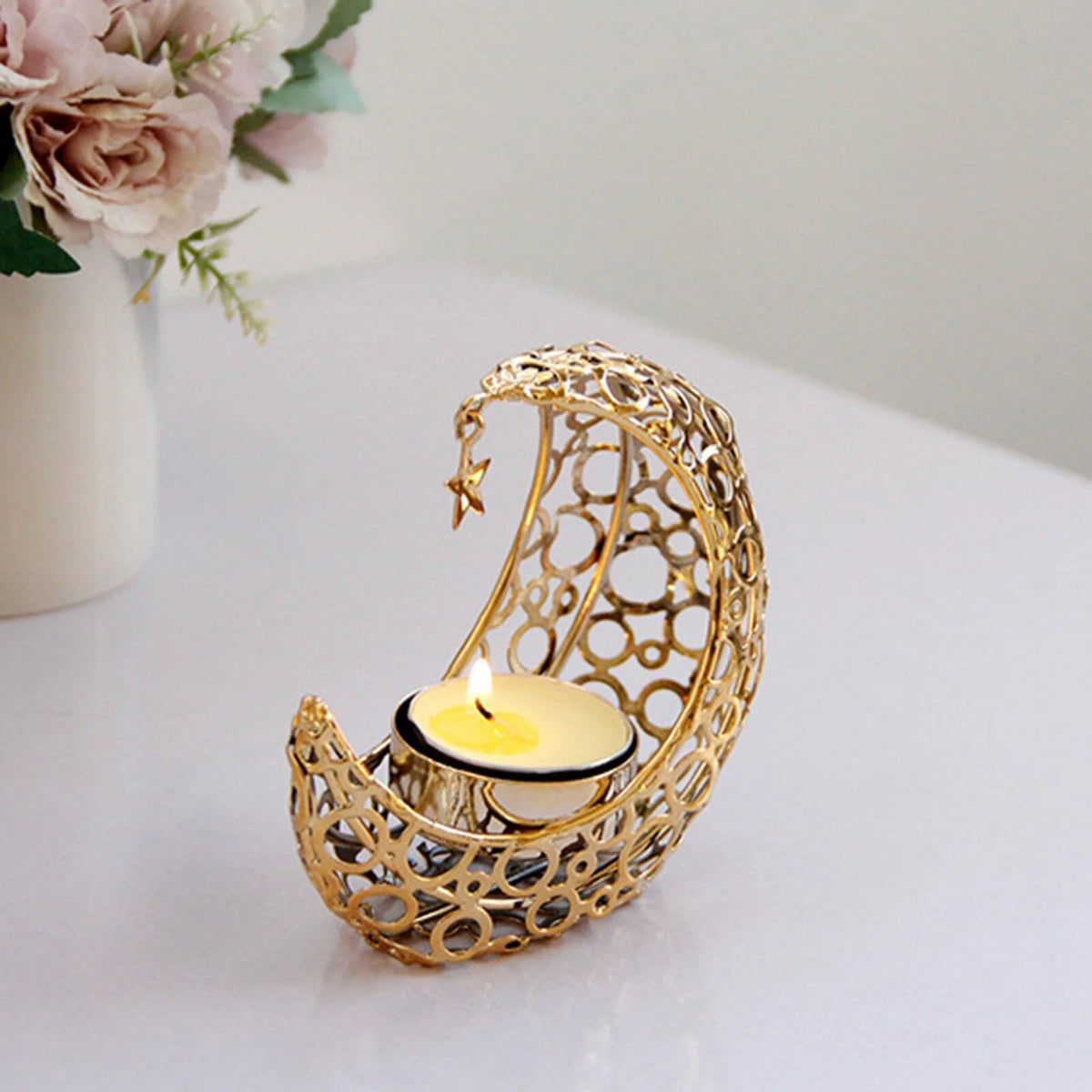 A golden crescent moon candle holder with a lit candle and a small star charm on a white surface.