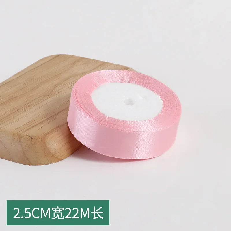 Pink silk satin ribbon roll with white padding and a wooden block for crafting
