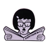 A black enamel pin badge featuring a cartoon character with short black hair looking surprised while reading a newspaper.