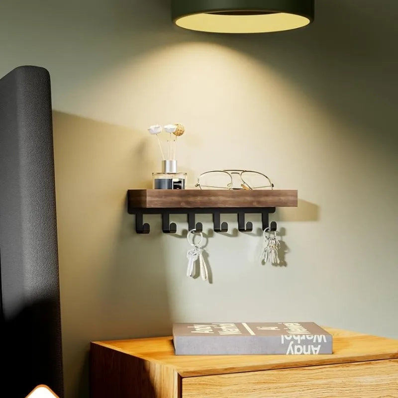 A rustic wooden floating shelf with hooks mounted on a light green wall above a wooden surface.