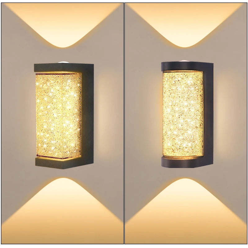 A pair of modern LED crystal outdoor wall sconces with a warm yellow light mounted on a light gray wall.